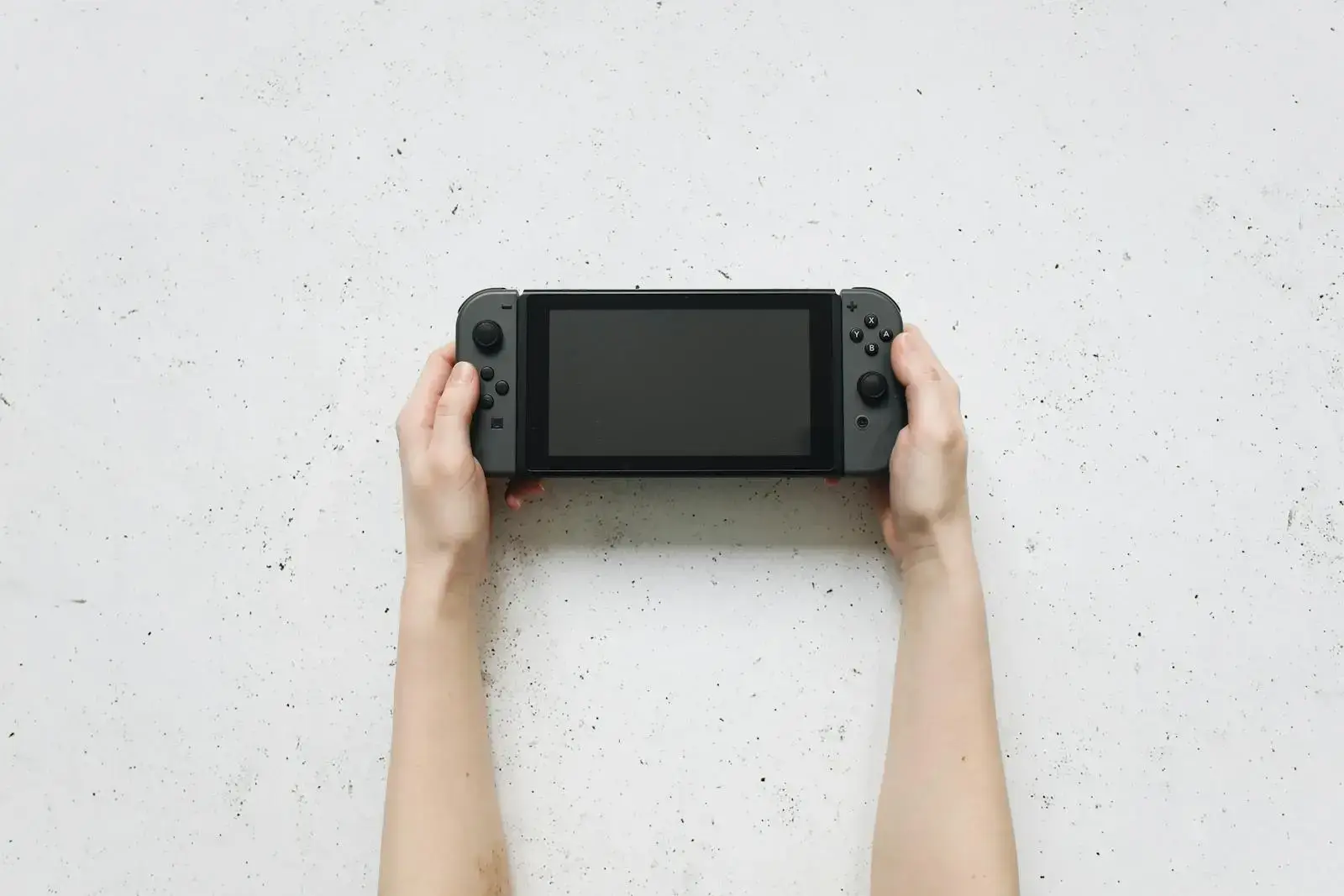 Top view of hands holding a portable gaming console against a textured white background.